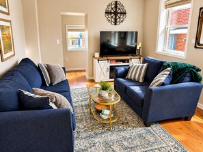 A living room with two sofas, a TV, and a decorative wall piece. - Shamrock Loft | Market St Frederick, MD (Frederick)