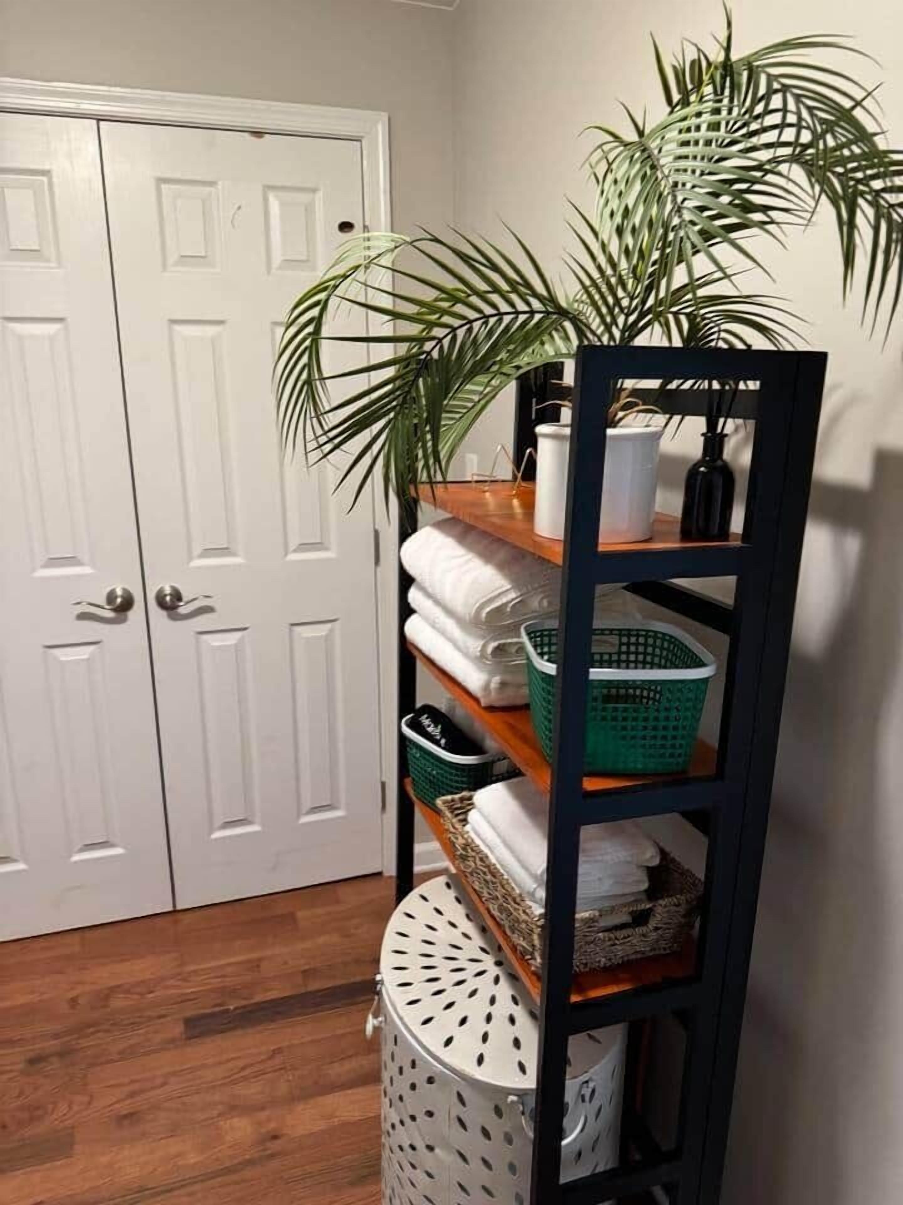 A hallway with a white door, a shelf with folded towels, a green basket, and a white laundry basket.