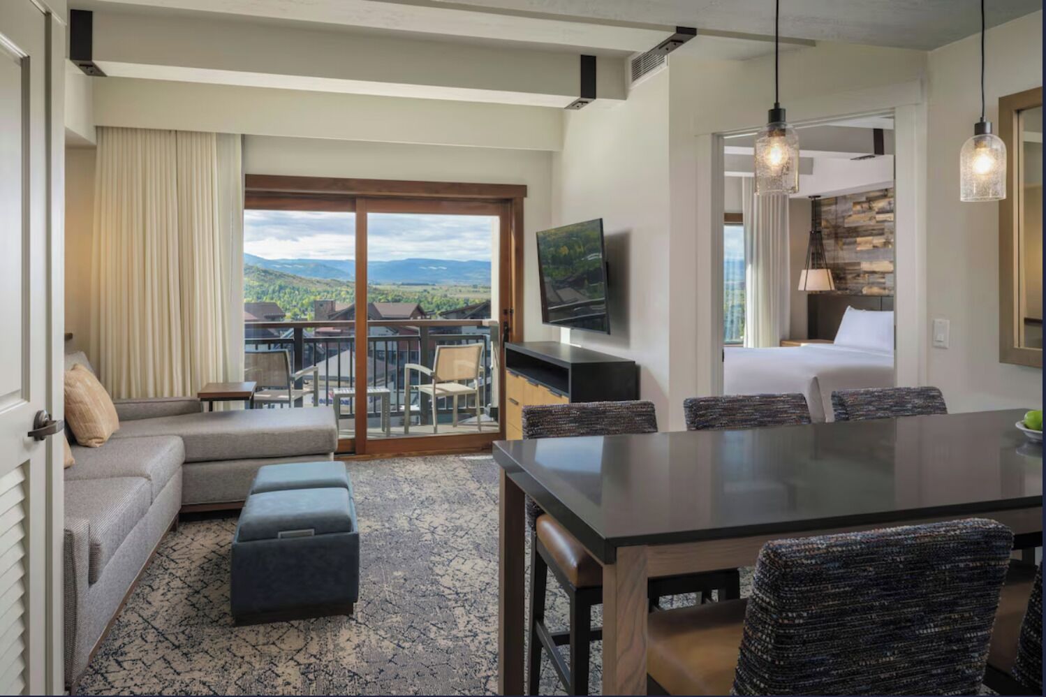 A hotel room with a balcony, a dining area, a television, and a bed.