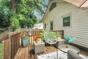 Une terrasse en bois, meublée pour l’extérieur, agrémentée de plantes en pot et offrant une vue sur une maison.