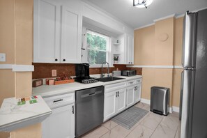 A modern kitchen with white cabinets, a stainless steel refrigerator, a dishwasher, and a window with blinds. - Cozy Modern Nook Near Downtown - Comfortable Home Away From Home (Montgomery)