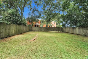 A fenced backyard with a grassy lawn and a brick building in the background. - Cozy Modern Nook Near Downtown - Comfortable Home Away From Home (Montgomery)