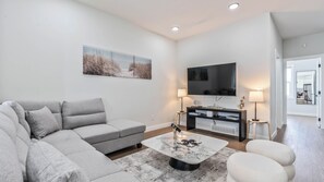 Uma sala de estar moderna com um sofá cinzento, uma mesa de centro e uma televisão de ecrã plano na parede.