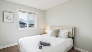 Ein Schlafzimmer mit einem Bett, einem Nachttisch, einer Lampe, einem Fenster und einem Wandbild.