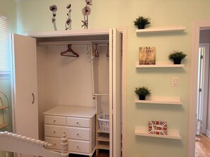 Ein Zimmer mit weißem Schminktisch, einem Kleiderschrank mit Platz zum Aufhängen und Regalen mit Dekoration.