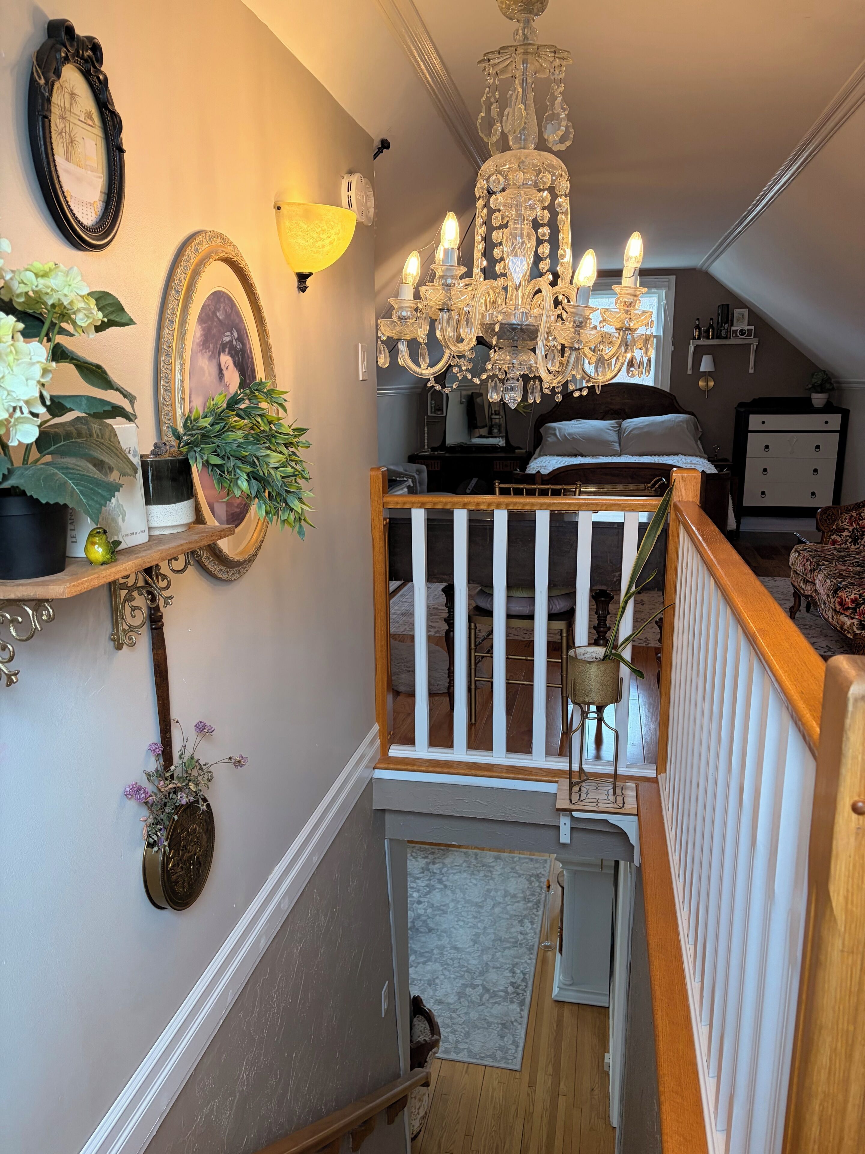 A staircase with a wooden railing, a chandelier, and wall-mounted decorations including framed pictures and a lamp.