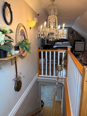 Eine Treppe mit hölzernen Geländern, einer Kristallleuchtre und Wandverzierungen, darunter gerahmte Bilder und eine Lampe.