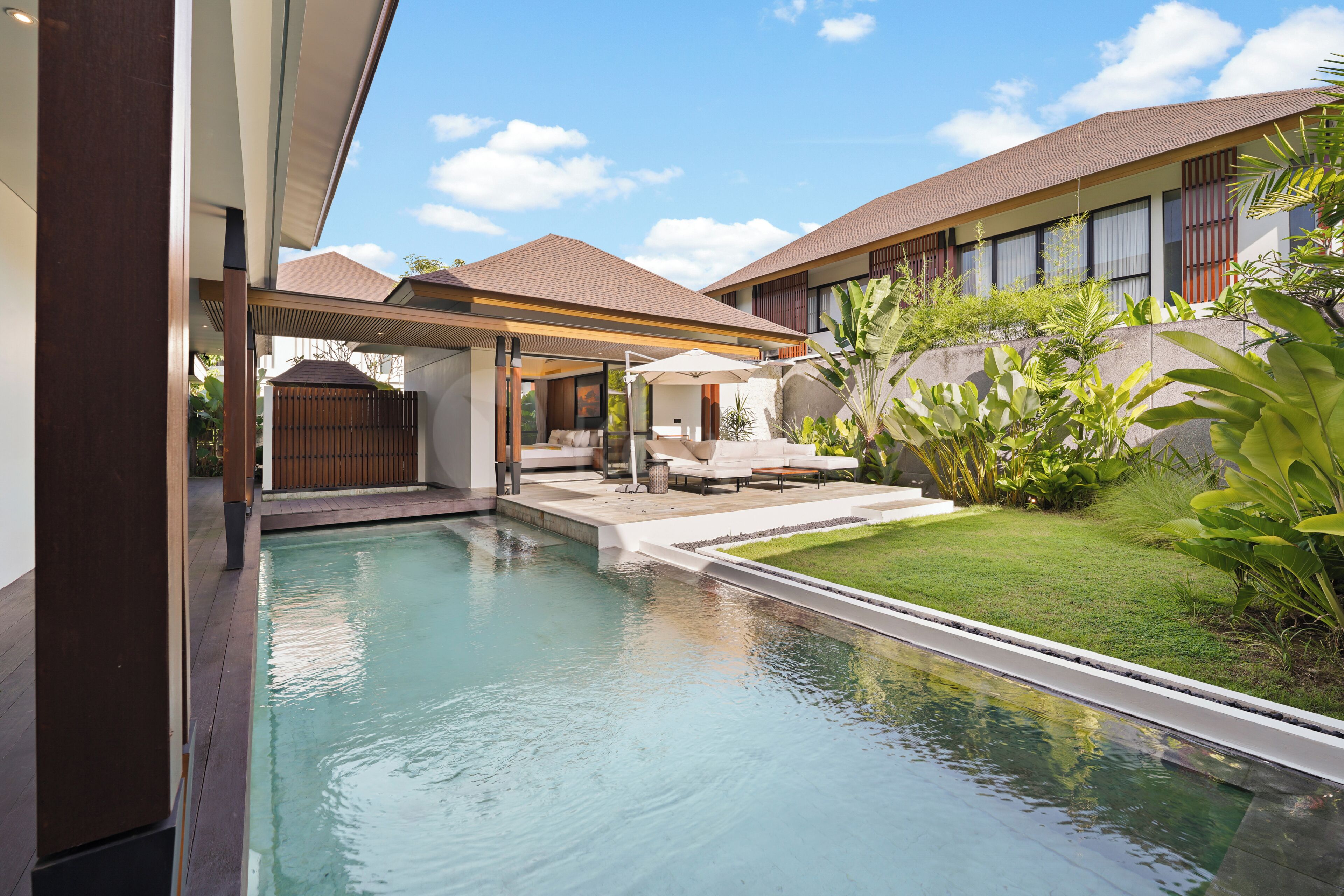 A modern pool area with a lounge, a covered seating area, and a well-maintained lawn.