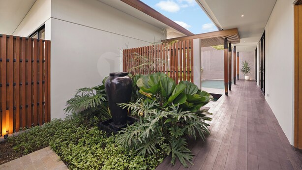 A modern outdoor space with a wooden fence, a large planter with various plants, and a pool area.