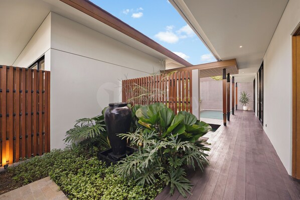 A modern outdoor space with a wooden fence, a large planter with various plants, and a pool area.