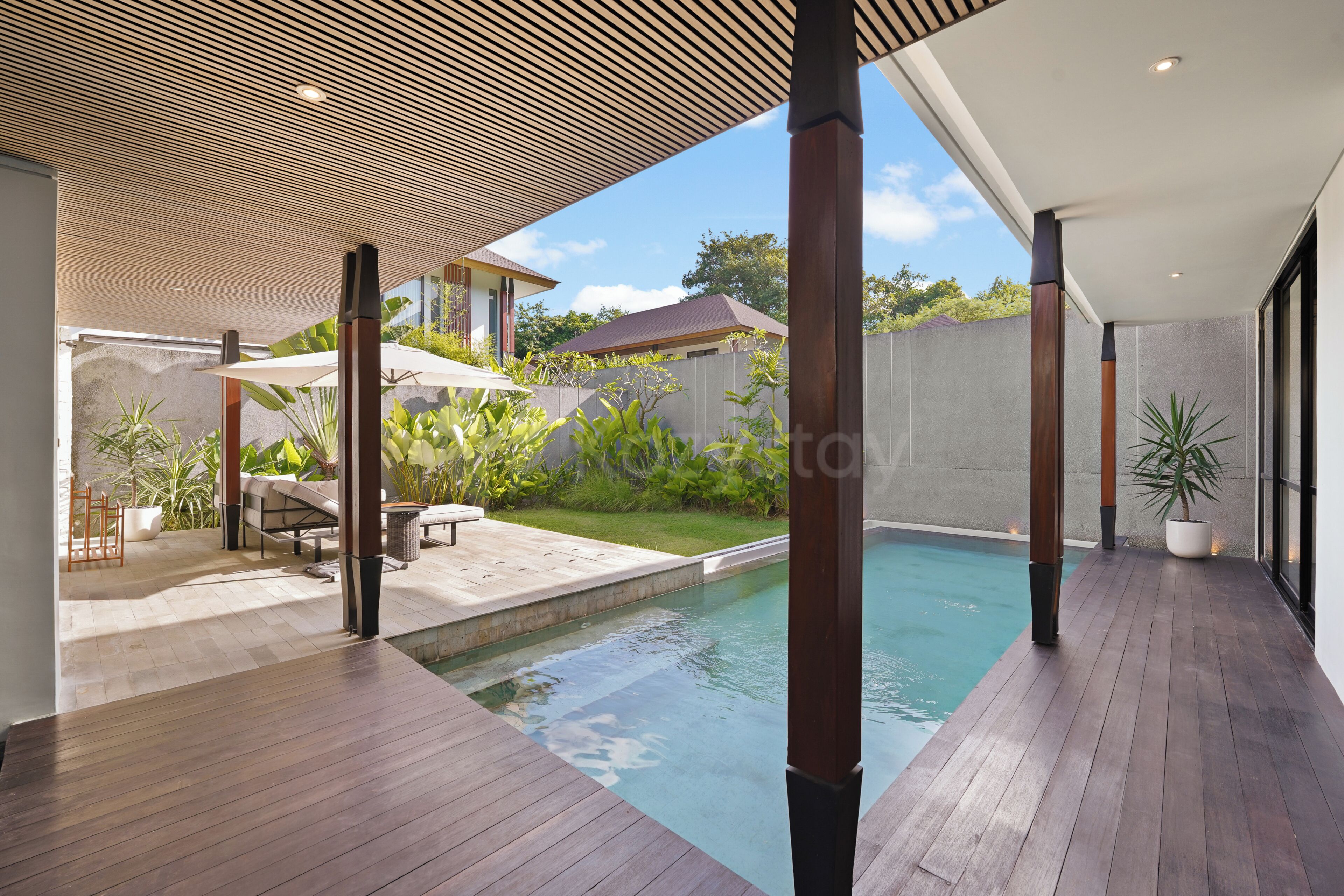 A modern outdoor pool area with wooden decking, lounge chairs, and umbrellas.