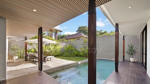 A modern outdoor pool area with wooden decking, lounge chairs, and umbrellas.