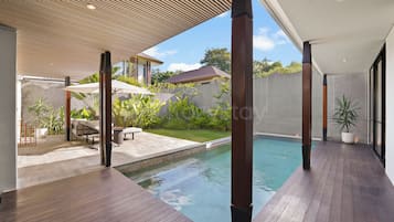 A modern outdoor pool area with wooden decking, lounge chairs, and umbrellas.