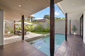 A modern outdoor pool area with wooden decking, lounge chairs, and umbrellas.