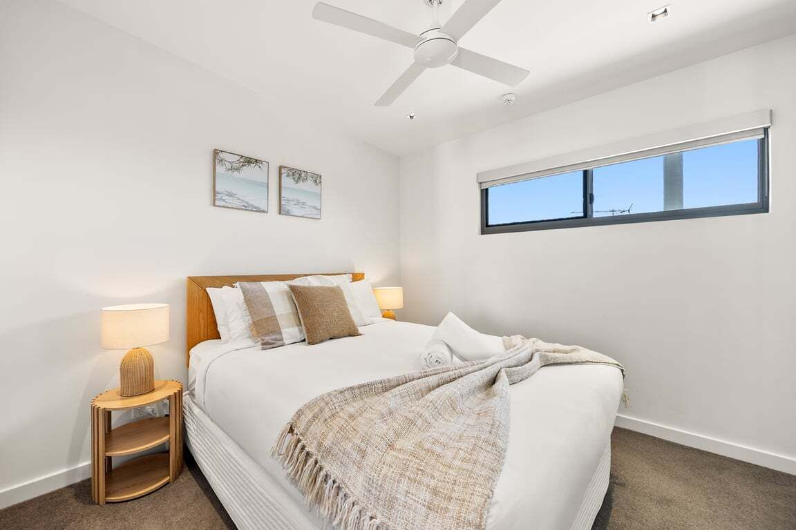 A bedroom with a bed, a ceiling fan, a window, and wall art.
