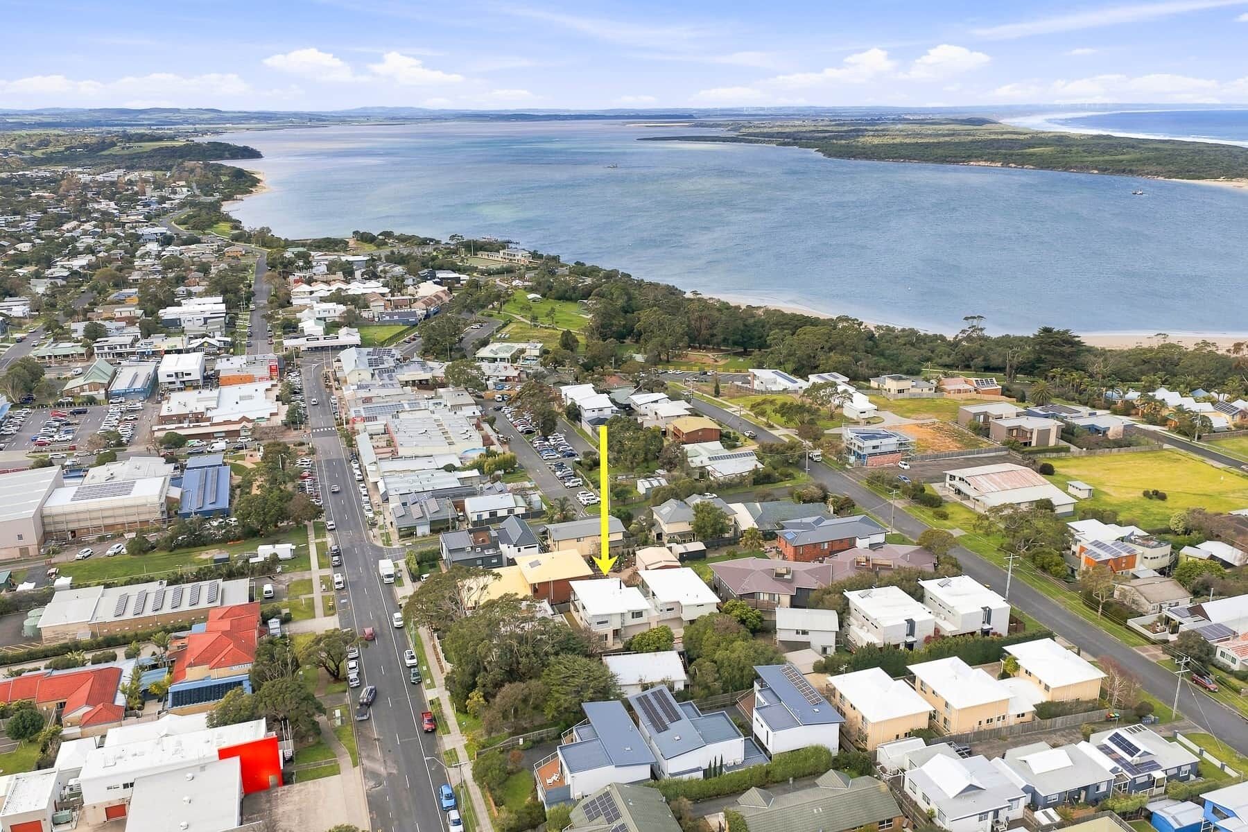 An aerial view of a coastal town with residential buildings, roads, and a large body of water.