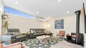 Uma sala de estar moderna com um sofá, uma poltrona e uma mesa de centro. Há uma lareira e um quadro na parede.