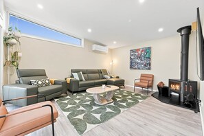A modern living room with a sofa, armchair, and a coffee table. There's a fireplace and a painting on the wall. - A'Beckett - Pets Welcome | Linen Included | Wifi (Inverloch)