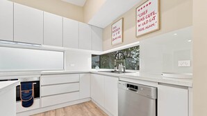 Uma cozinha moderna com armários brancos, uma lava-louças Bosch e janela com vista para o verde.
