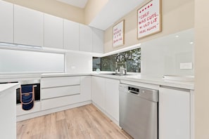 A modern kitchen with white cabinetry, a Bosch dishwasher, and a window overlooking greenery. - A'Beckett - Pets Welcome | Linen Included | Wifi (Inverloch)