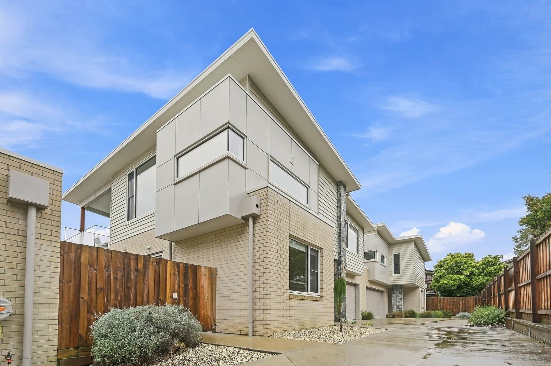 A modern two-story house with a sloped roof, a brick facade, and a wooden fence.
