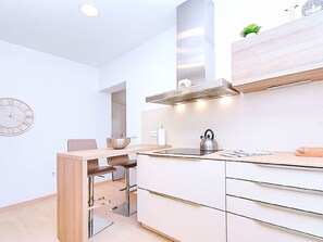 A modern kitchen with a built-in stove, a kettle, and a wooden shelf above the counter. - LOS PINOS - VILLA 7 by Interhome (El Carmoli)