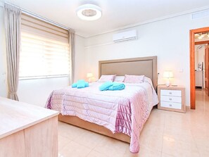 Quarto de hotel com cama, mesas de cabeceira, escrivaninha e janela com cortinas.