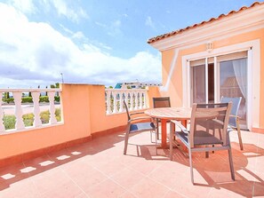 Uma varanda com mesa e cadeiras, uma porta de vidro deslizante e vista para o céu.