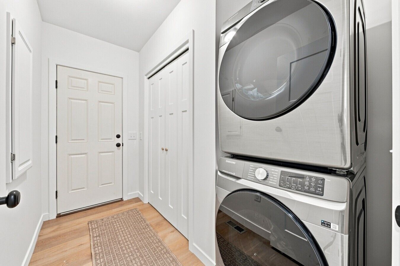 A laundry room with stacked washers and dryers, a white door, and a wooden floor.
