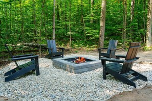 A fire pit with two Adirondack chairs in a forest setting. - Private 5-Acre Retreat with Hot Tub, Sauna + Fire Pit (Bellaire)