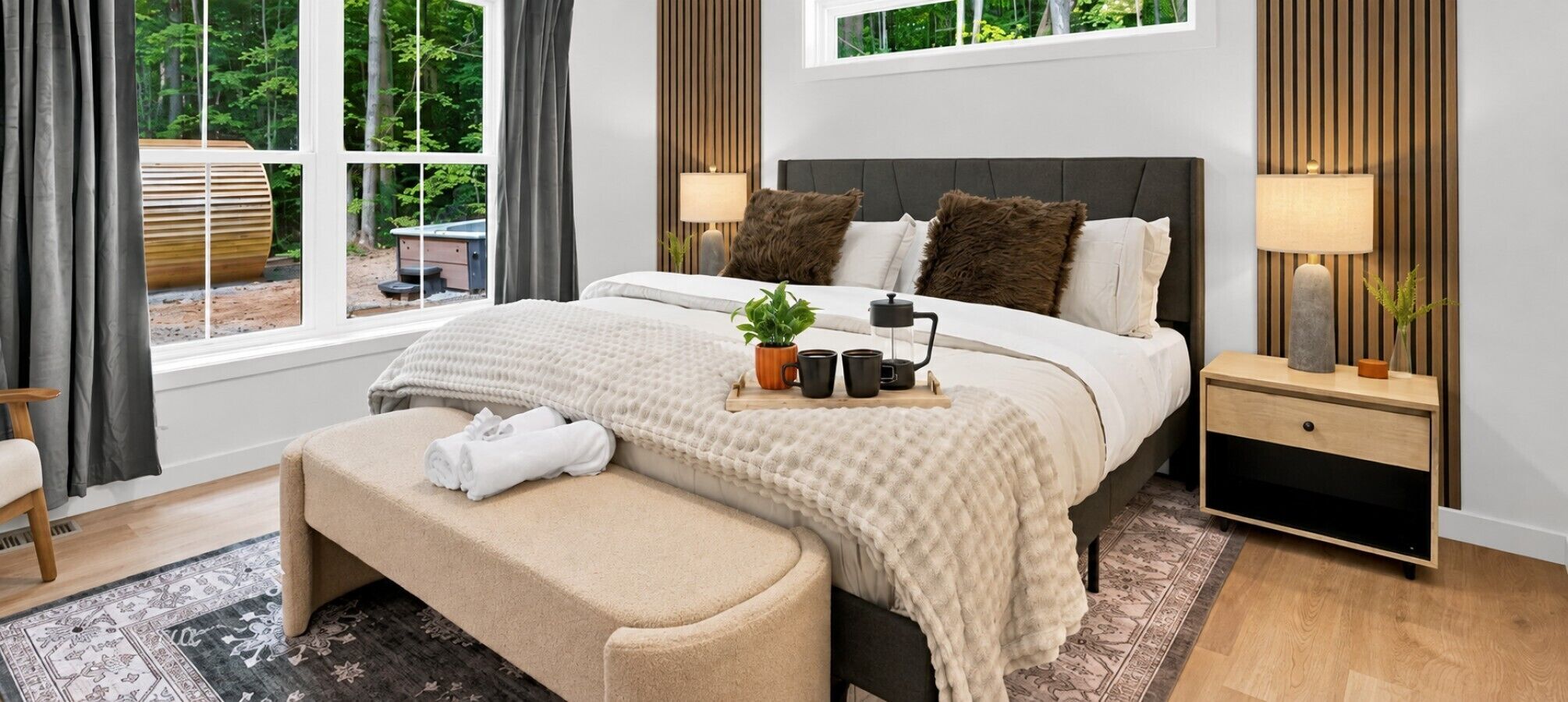 A modern bedroom with a large bed, bedside tables, a bench, and a view of the outdoors.