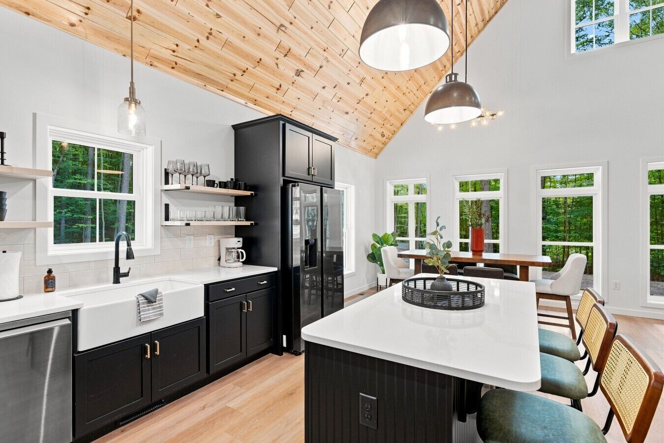 Cocina moderna con gabinetes negros, encimera blanca y una isla grande. Varias ventanas ofrecen luz natural y vistas a zonas verdes.