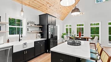 Cocina moderna con gabinetes negros, encimera blanca y una isla grande. Varias ventanas ofrecen luz natural y vistas a zonas verdes.