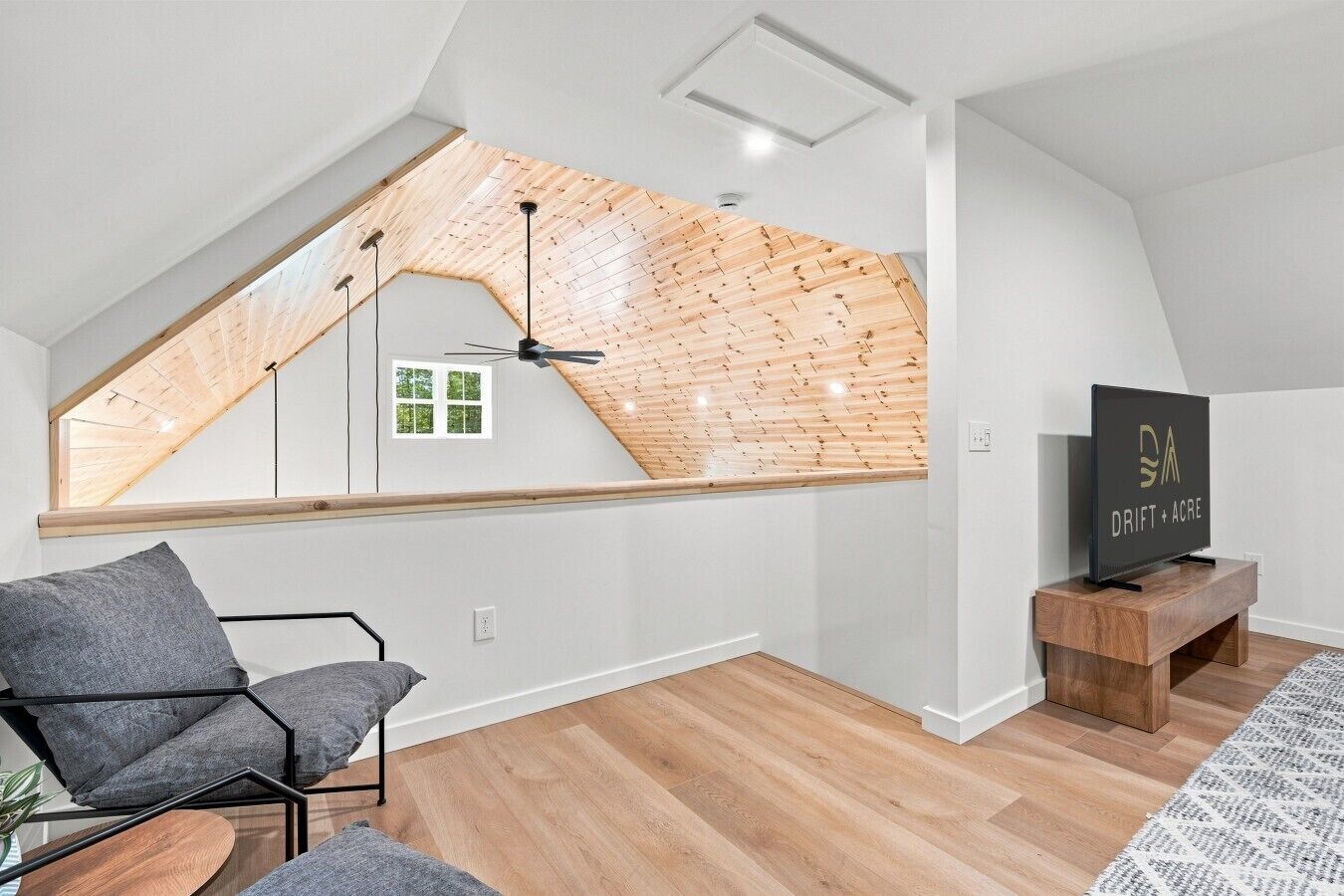 A modern loft apartment with a sloped ceiling, a skylight, a black TV on a wooden stand, and a grey sofa.
