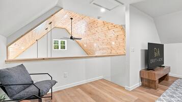 A modern loft apartment with a sloped ceiling, a skylight, a black TV on a wooden stand, and a grey sofa.