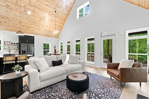 A spacious living area with a high ceiling, a modern kitchen, and large windows offering views of the outdoors. - Private 5-Acre Retreat with Hot Tub, Sauna + Fire Pit (Bellaire)