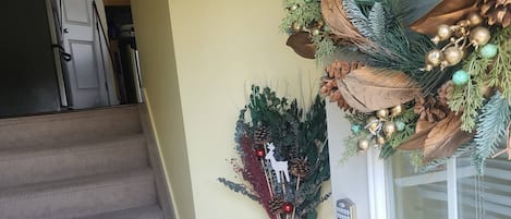 Eine Treppe führt zu einer Tür, geschmückt mit einem dekorativen Kranz und einem kleinen Tisch mit einer Vase und einem Rentier-Ornament.