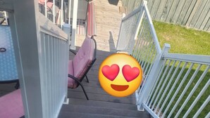 A wooden deck with a metal railing, a pink chair, and a small table. - Shalom Casablanca Home (Edmonton)