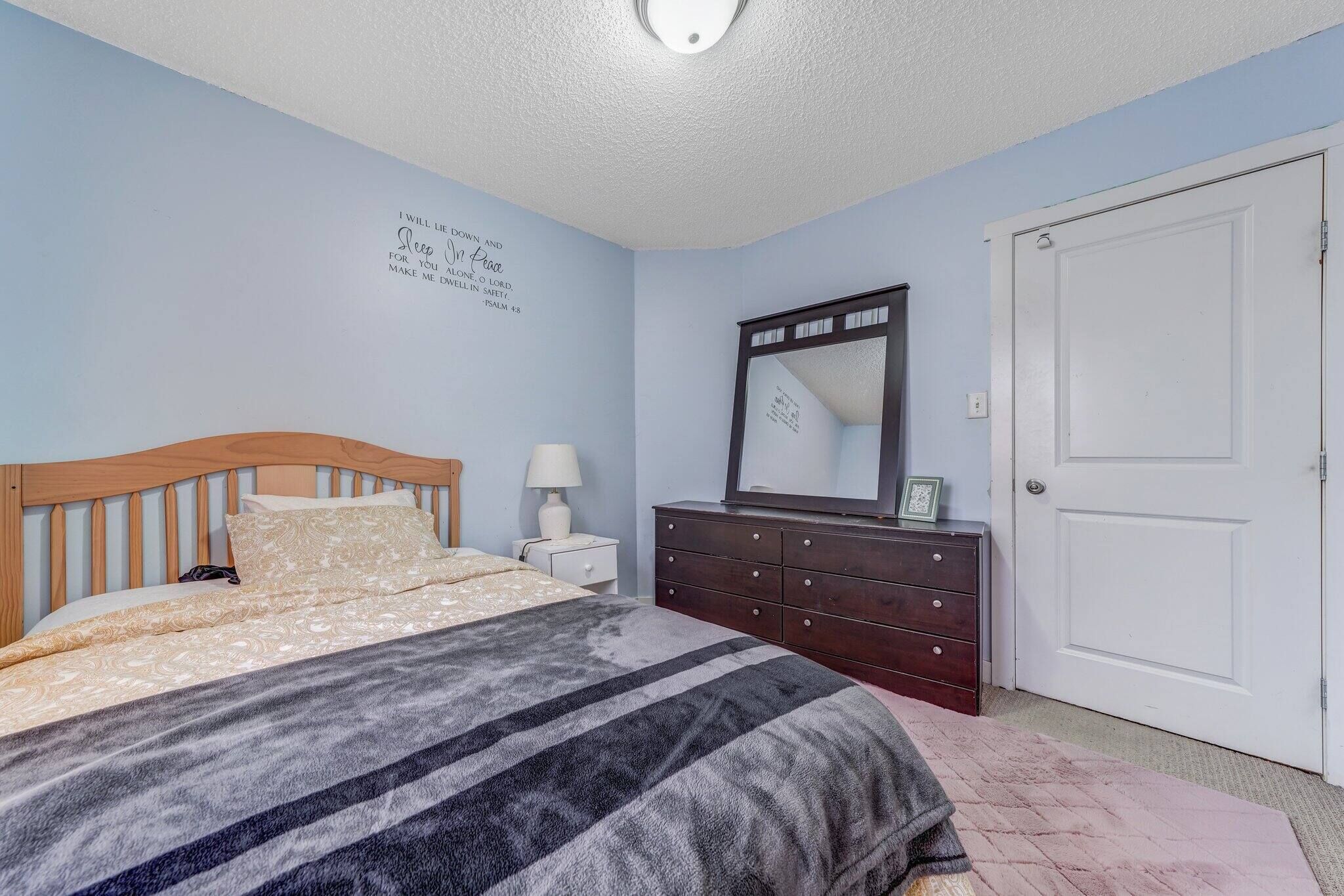 Een slaapkamer met een bed, een ladekast, een spiegel en een deur.