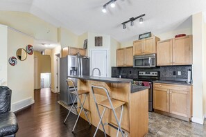A modern kitchen with wooden cabinets, stainless steel appliances, and a bar area with stools. - Shalom Casablanca Home (Edmonton)