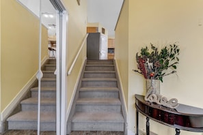 Una escalera conduce a una zona de cocina con una planta decorativa sobre una consola.