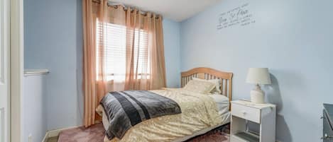 A bedroom with a bed, a nightstand, a lamp, and a wall with a religious quote.