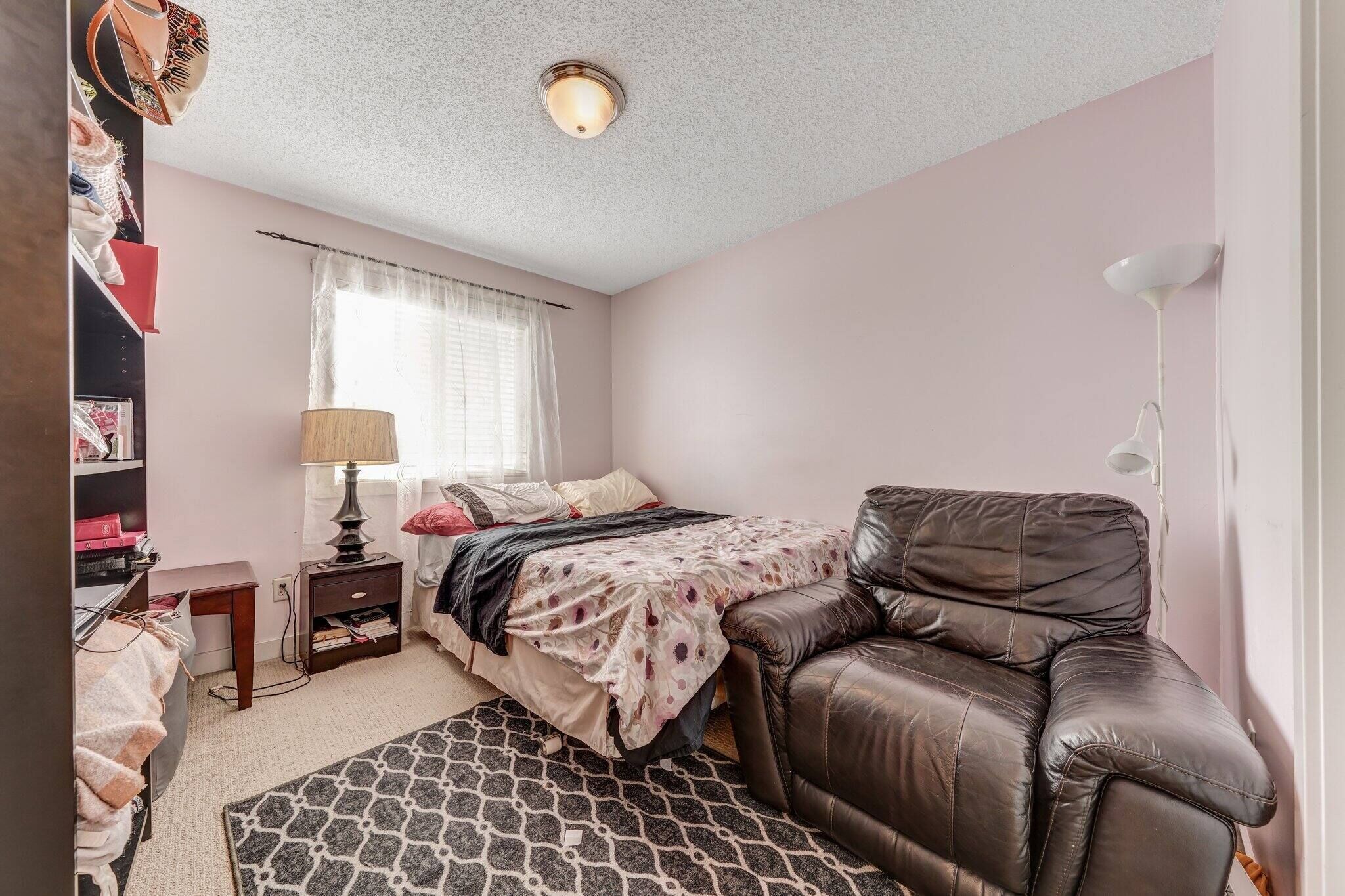 A bedroom with a bed, a leather sofa, a bedside table, a lamp, and a window with curtains.