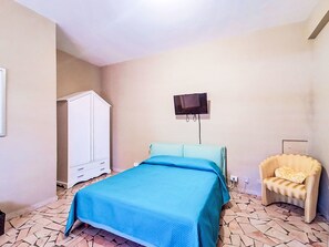Een slaapkamer met een bed, een televisie aan de muur, een kledingkast en een stoel.