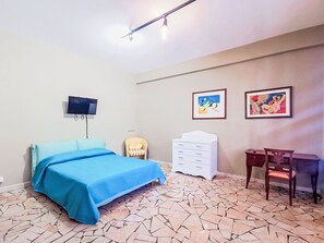 Ein Zimmer mit einem Bett, einem Fernseher, einem Schreibtisch und zwei gerahmten Bildern an der Wand.