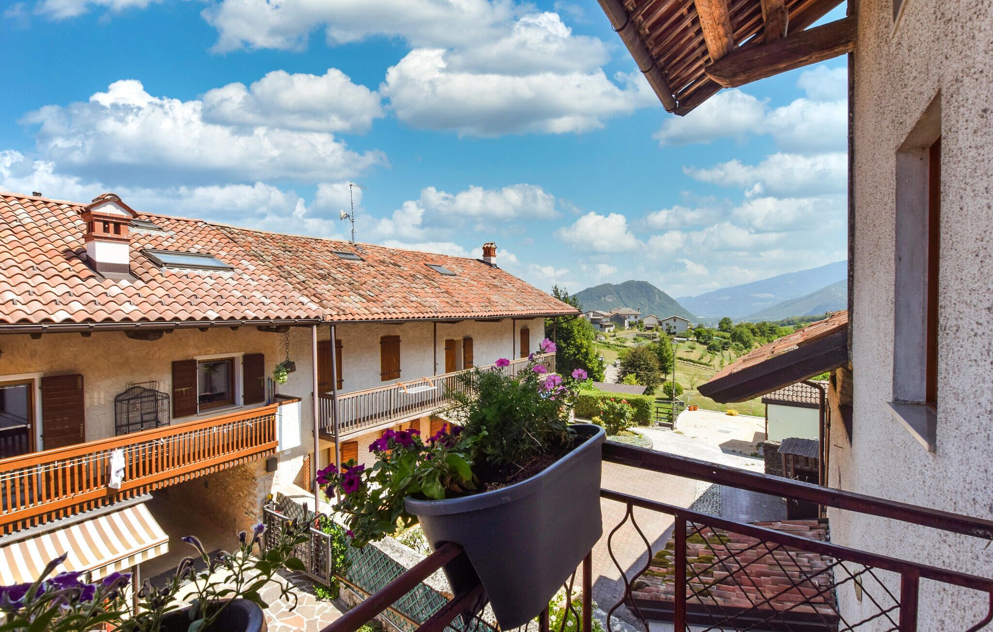 A balcony with a view of a terracotta-roofed building, a potted plant, and a clear sky.