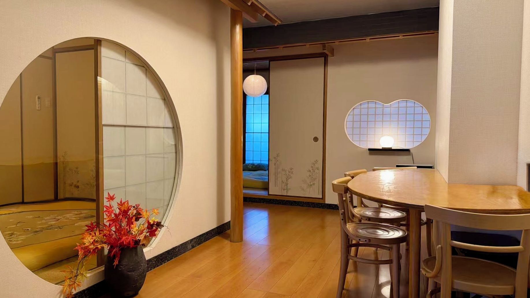 A traditional Japanese room with tatami flooring, a low table with chairs, a shoji screen, and a hanging light fixture.