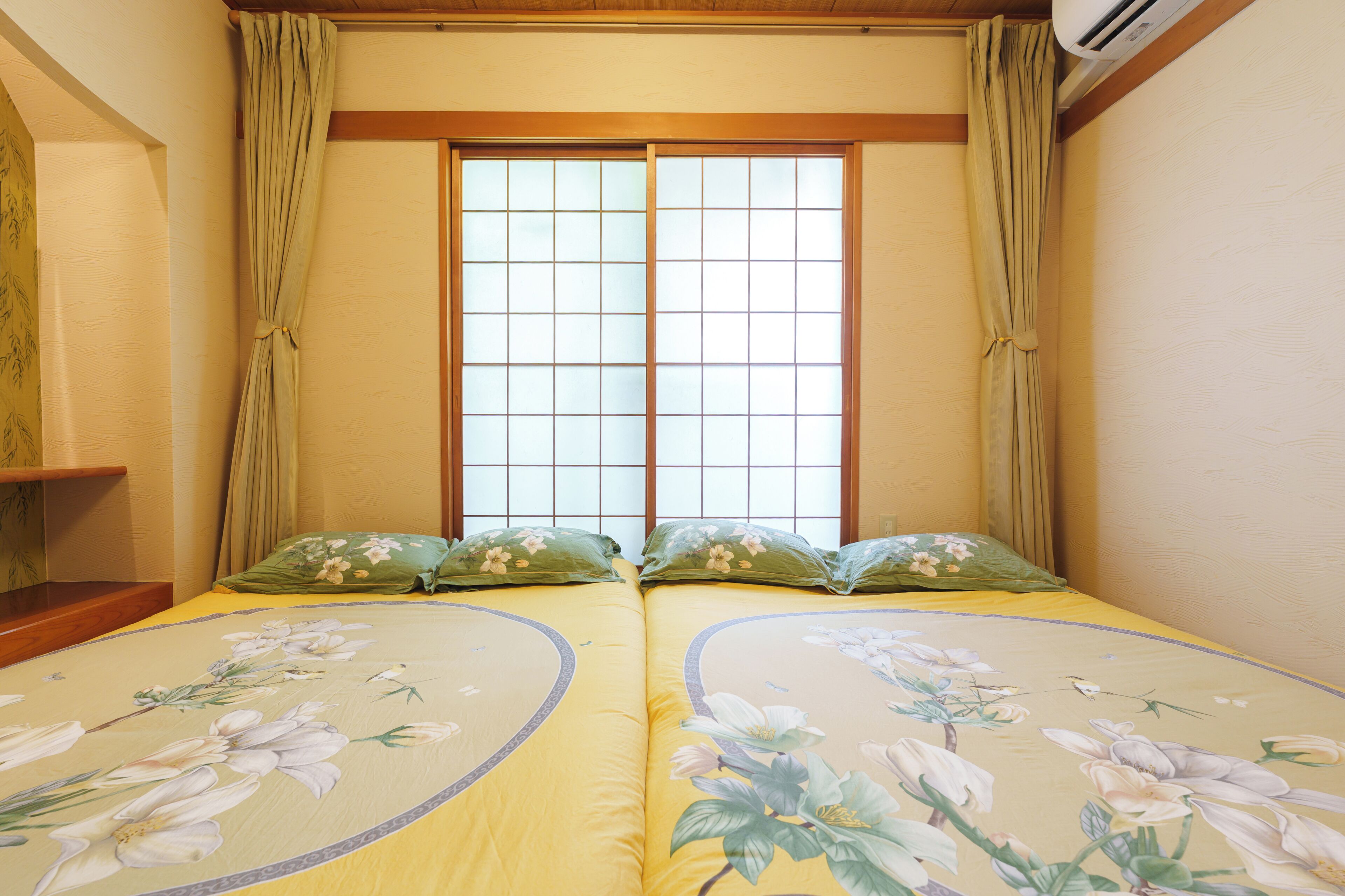 A room with two beds, a window with a grid pattern, and a wooden ceiling.