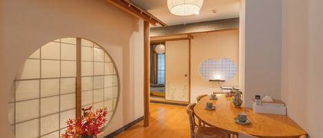 A traditional Japanese interior with a wooden dining table, chairs, a large shoji screen, and a hanging light fixture.