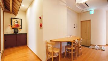 A room with a wooden floor, a round table with chairs, a framed picture on the wall, and a door with a wooden panel.
